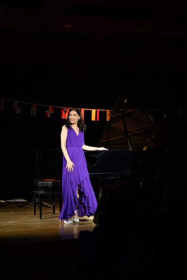 Femme en robe violette se tenant près d'un piano sur scène.